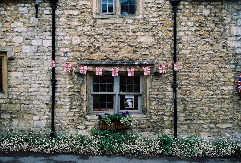 Rustic stone facade of a traditional British house with flag bunting and flowers.